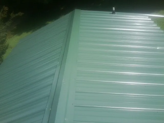 New green metal panels meeting at the ridge of a roof — Flat Roof Repair work by our crew in Mount Vernon